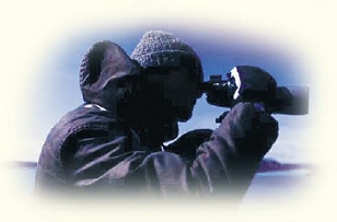 [PHOTO: Man observing something through binoculars]