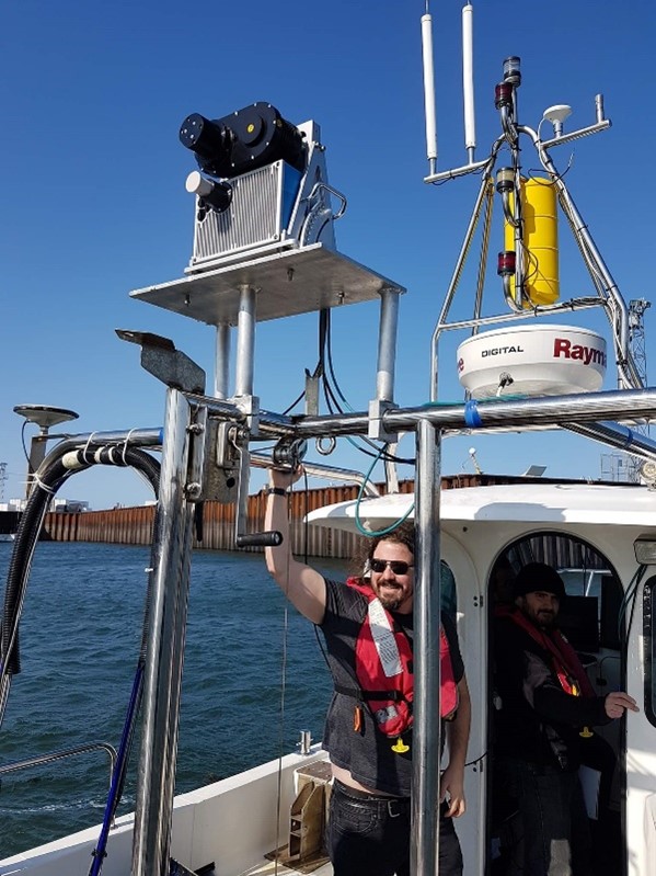 Guillaume Labbé-Morissette, Ocean Decade Champion for An Accessible Ocean, Director of IT Research and Development at CIDCO in Rimouski, Quebec. Guillaume wears a PFD and sunglasses and is standing aboard a research vessel at sea on a sunny day.